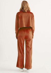 Gekürzte braune Cord-Jacke und passende weite Hosen, die aus einem strukturierten Stoff und einem elastischen Bund gefertigt sind, kombiniert mit weißen Sneakers.