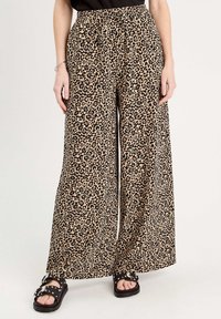 Pantalon large à imprimé léopard en tissu léger, avec une ceinture élastique et une coupe décontractée. Sandales noires en dessous.