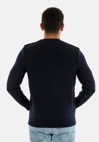Maglione lavorato a maglia blu navy con collo rotondo, polsini e orlo a costine, e dettagli sulle spalle. Il materiale appare morbido e strutturato.