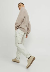 Maglione beige oversize, pantaloni cargo bianco sporco con tasche laterali e scarpe in suede color tan con suola marrone. Design semplice, tessuto leggero.