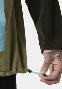 Fleece-Schicht in Olivgrün mit einem blauen Nylonpanel. Verfügt über einen Kordelzug am Saum und schwarze Bündchenakzente. Handbetätigter Zugkordel.