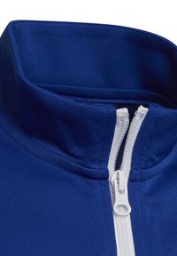 Primer plano de un cuello de chaqueta azul con una cremallera blanca parcialmente subida, mostrando una tela texturizada y costuras resistentes.