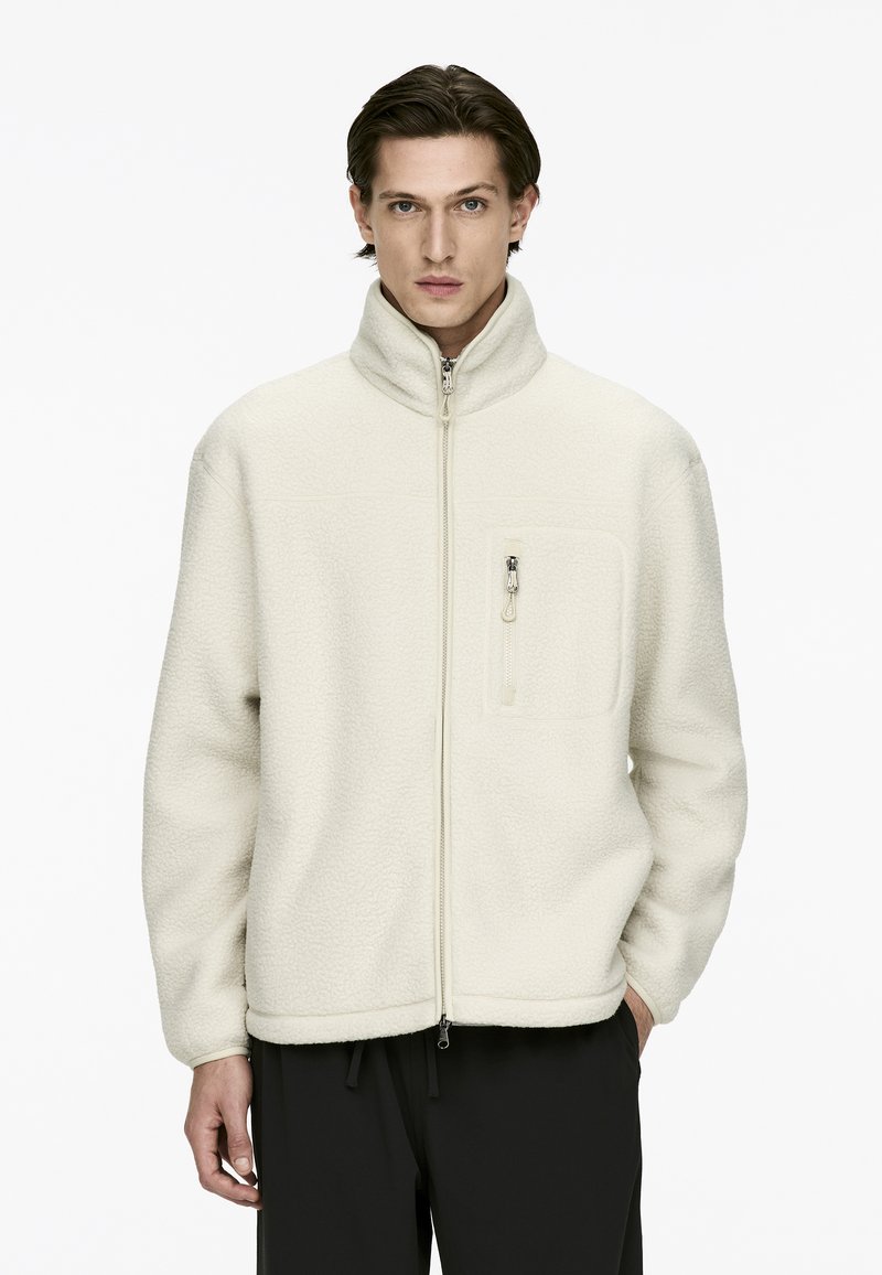 Off-white fleece jacket with high collar, front zip, and a zippered chest pocket. Features a textured surface and elasticized hem.