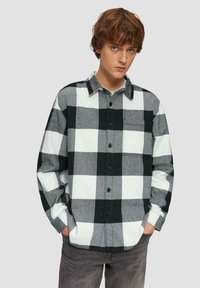 Zwart-wit geblokt flanel shirt met een knoopsluiting, lange mouwen en een borstzak; gemaakt van zachte geweven stof.