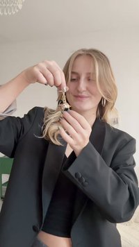Gold-tone keychain with a cat charm, featuring black and white enamel details and colorful accents. The background shows a light-colored wall.