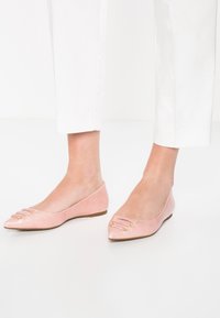 Ballerine in pelle rosa con punta affusolata, decorate con tre anelli dorati sulla parte superiore e una suola profilata bassa.
