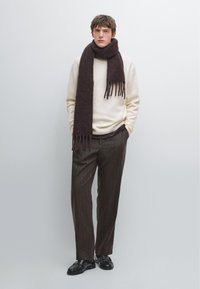Tröja i krämfärgad stickning, kombinerad med bruna randiga byxor. Mörkbrun fransad scarf ger textur, kompletterad med svarta loafers.