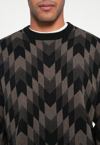 Czarny i brązowy sweter z wzorem w jodełkę, z prążkowanym dekoltem i teksturowaną dzianiną.