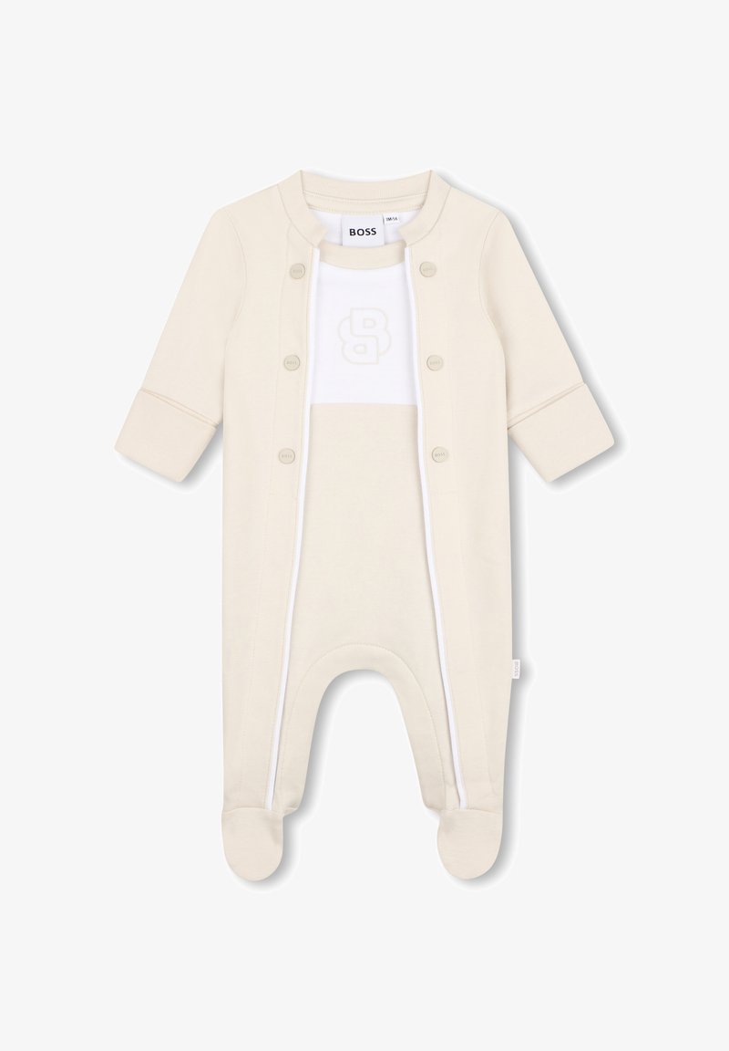 Combinaison pour bébé couleur crème avec pieds, manches longues, boutons-pression à l'avant, panneau blanc sur la poitrine et logo "B" embossé.