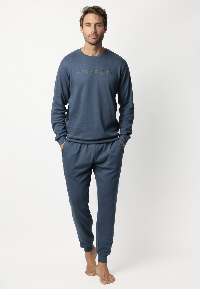 Conjunto de ropa de casa de color azul oscuro que incluye una camiseta de manga larga con un logo y pantalones con cintura elástica y puños en los tobillos. Tejido suave y liso.