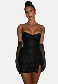 Robe mini noire à sequins avec des bretelles spaghetti réglables, encolure cœur et fente sur le côté. Des gants noirs transparents complètent le look.