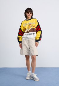 Colorful sweatshirt with yellow and black stripes, graphic print, paired with beige shorts. Grey sneakers with white accents.