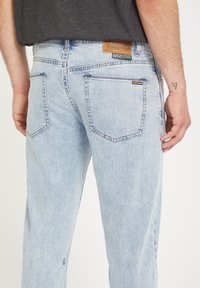 Lichtblauwe denim jeans met een ontspannen pasvorm, voorzien van twee achterzakken en een bruine leren patch met branding op de tailleband.