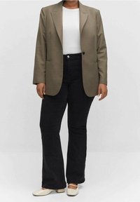 Blazer écossais marron avec épaulettes, t-shirt blanc en dessous, associé à un jean flare noir et des chaussures à talons blocs crème.