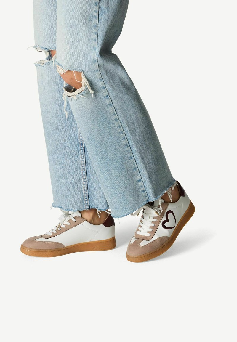 Sneaker mit einem beige-, weiß- und braunfarbenen Design; aus Wildleder und Leder; runde Zehenpartie; auffälliges Herzdesign; Gummisohle.