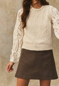 Woven kremowy sweter z koronkowymi puff rękawami i dzianinowym wykończeniem, zestawiony z brązową mini spódnicą w kratę. Teksturowana dzianina i wzorzyste akcenty.