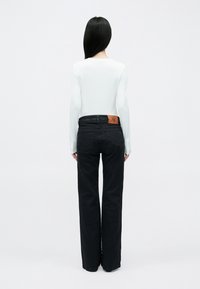 Fekete, széles szárú farmernadrág barna bőr logó folttal a hátoldalán, fehér, testhezálló, hosszú ujjú felsővel párosítva.