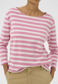 Rozā un baltas svītrains garām piedurknēm tops ar laivas kakla izgriezumu un mīkstu, elpojošu audumu. Kombinēts ar bēšām biksēm.