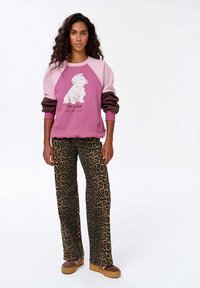 Růžová a hnědá mikina s grafikou psa a textem "ZAMILOVÁN", v kombinaci s leopardími zvonovými kalhotami a hnědými botami.