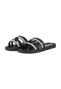 Schwarze Riemchensandalen mit drei schmalen Riemen, die mit silbernen Glitzerdetails versehen sind. Flache Sohle mit strukturierter Oberfläche für Grip. Leichtes Design.