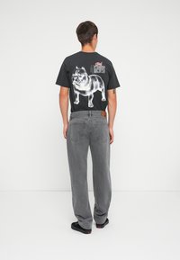 Sort grafisk t-shirt med et stort hundetryk på ryggen. Bæres med løstsiddende, grå jeans og sorte sko.