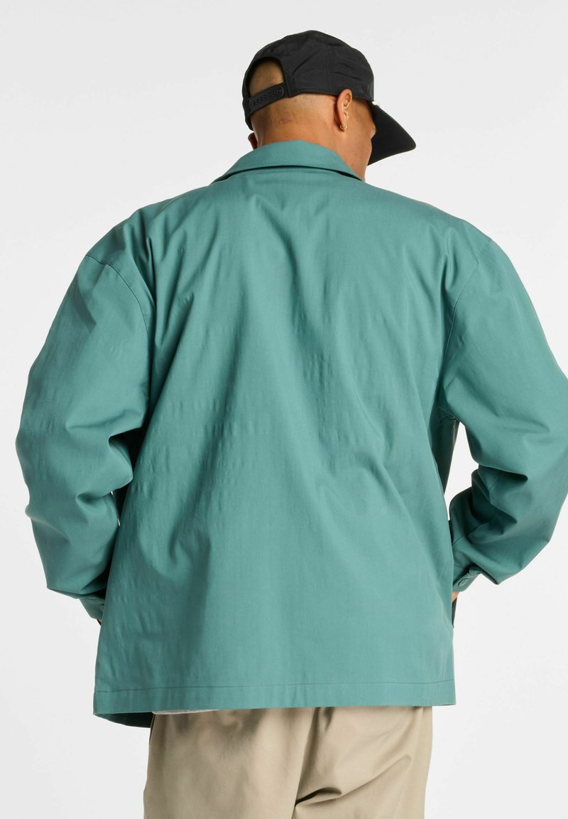 Hellgrüne Jacke mit lockerem Sitz, langen Ärmeln und einem Kragen. Verfügt über eine glatte Textur und einen geraden Saum auf Taillenhöhe.