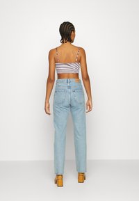Top cropped listrado com alças finas; jeans de cintura alta azul claro com bolsos traseiros e um patch na cinta; sapatos bege.