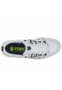 White leather sneaker with black accents and laces. Features a rounded toe, perforated front, and green logo on a black insole.