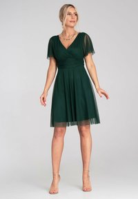 Grünes Kleid mit gefaltetem Rock, kurzen durchsichtigen Ärmeln und tiefem V-Ausschnitt. Hergestellt aus leichtem Stoff für ein fließendes Erscheinungsbild.