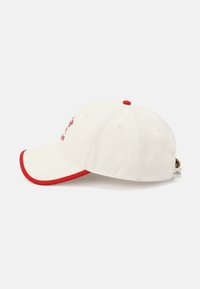 Witte knupp pet met een gebogen rode rand en rode accenten. Heeft stiksel en een label aan de zijkant. Stof is glad en gestructureerd.