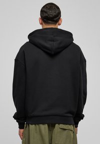 Czarna bluza z kapturem wykonana z miękkiej bawełnianej mieszanki. Charakteryzuje się luźnym krojem, opuszczonymi ramionami oraz ściągaczami na rękawach. Gładka faktura, bez nadruków.