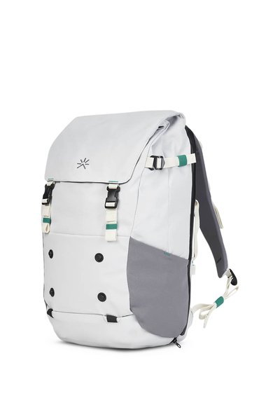 Mochila gris y blanca con cierre tipo solapa, correas ajustables, botones frontales y un acento de tela azul verdoso y gris. Presenta un diseño limpio.