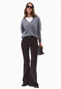 Szary sweter w serek z luźnymi rękawami, połączony z brązowymi spodniami z sztruksu o wysokim stanie i rozszerzanymi nogawkami. Uzupełniony małą torebką w wzory.