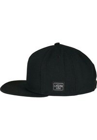 Svart caps laget av kraftig stoff med flat skjerm og en merkepatch på siden. Har sydd detaljer og snapback-lukking.