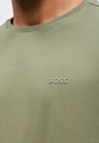 Olivovo zelené tričko z textúrovaného bavlneného materiálu s malým béžovým logom "BOSS" na ľavej strane hrude a okrúhlym výstrihom.