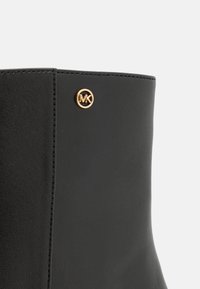 Čierne ankle boot s umelou kožou s elegantným dizajnom, hladkou textúrou a zlatým logom na boku.