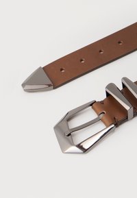 Cintura in pelle marrone con fibbia geometrica in metallo argentato e punta, posata su una superficie bianca.