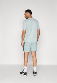 Αθλητική μπλούζα ανοιχτού μπλε χρώματος και σορτς που ταιριάζουν, με μαύρες πλαϊνές ρίγες, συνδυασμένα με μαύρα αθλητικά παπούτσια και λευκές κάλτσες. Μινιμαλιστικός σχεδιασμός.