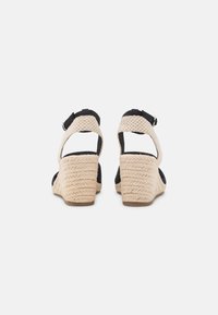 Sandali con tacco a cuneo neri con tacco in stile juta intrecciata, cinturino alla caviglia regolabile e retro aperto. Presentano un tessuto testurizzato e accenti di colore contrastanti.
