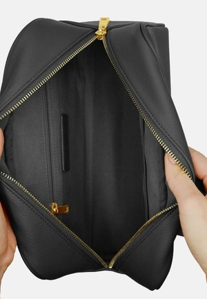 Sac à main en cuir noir avec une fermeture éclair dorée, ouvert pour révéler un intérieur spacieux et une petite poche. Texture lisse et forme structurée.
