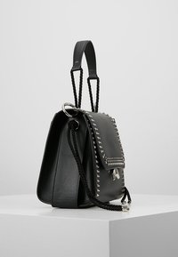 Mustaan nahkakäsilaukku, jossa on rakenteellinen muotoilu, koristeelliset hopeiset niitit kannessa, letitetyt hihnat ja sivussa hopeinen rengasdetali.