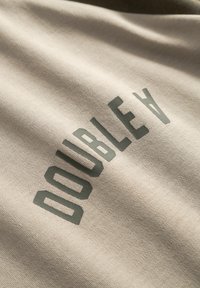 Beež kangas, millel on matirohelised tähed, mis moodustavad sõna "DOUBLE A." Tekstuur on sile ja kergelt reljeefne, trükise lähedalt vaadatuna.