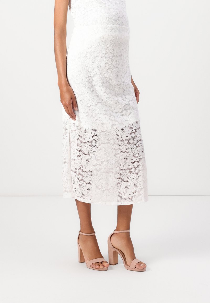 Abito midi in pizzo bianco, con motivo floreale, sezione inferiore semi-trasparente. Un paio di sandali con tacco a blocco rosa chiaro e cinturini alla caviglia.