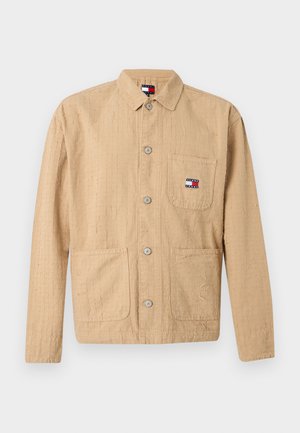 Chaqueta beige de manga larga con textura, cierre frontal con botones, tres bolsillos y pequeño logo de Tommy Jeans en el bolsillo del pecho y etiqueta del cuello.