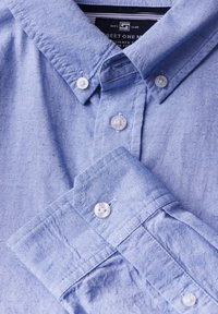 Light blue button-up shirt with a textured fabric, featuring small dotted patterns and white plastic buttons on the collar and cuffs.
