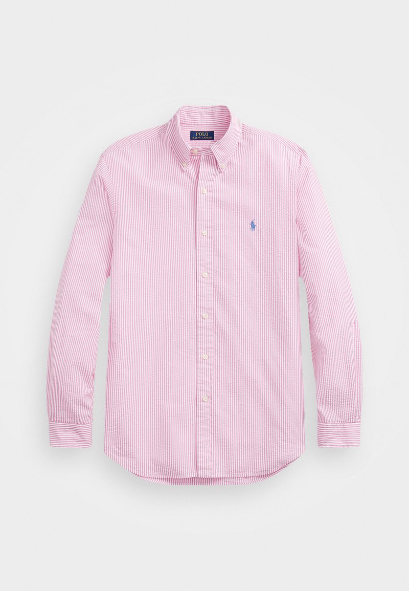 Šviesiai rožinė mygtukinė marškinėliai su baltais vertikaliais dryžiais ir mažu mėlynu logotipu ant kairės krūtinės pusės. Turi apykaklę ir ilgas rankoves.