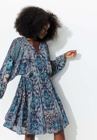 Robe fluide à motifs dans des tons bleus et turquoises, avec un décolleté en V, des manches longues et des motifs floraux et géométriques détaillés.