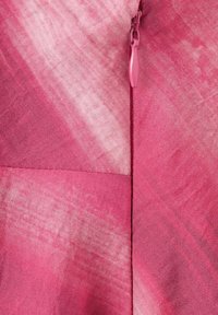 Zbliżenie na różowy materiał z pionowym zamkiem błyskawicznym w tym samym kolorze, ukazującym strukturę i subtelne różnice w odcieniach.