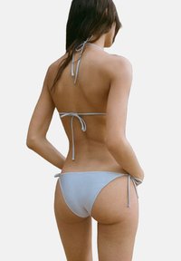 Light blue bikini with a halter neck and rear tie closure. The fabric is smooth and fitted, featuring minimal coverage on the bottom.