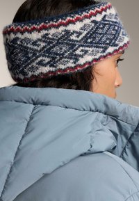 Neulottu pääpanta laivastonsinisenä, punaisena ja valkoisena geometrisella kuviolla; yhdistetty vaaleansiniseen toppatakkiin, jossa on sileä pinta.